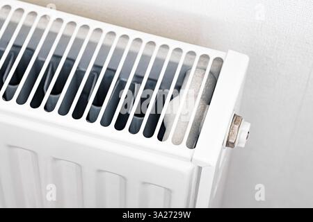 Nahaufnahme eines alten weißen Heizkörpers mit Heizventil und Metallrohren mit Anzeichen von Verschleiß. Eine detaillierte Aufnahme, die die Heizung und den Energieverbrauch des Hauses veranschaulicht Stockfoto