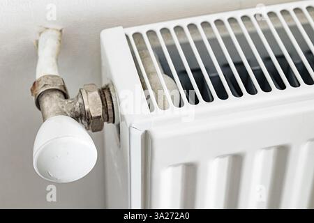 Nahaufnahme eines alten weißen Heizkörpers mit Heizventil und Metallrohren mit Anzeichen von Verschleiß. Eine detaillierte Aufnahme, die die Heizung und den Energieverbrauch des Hauses veranschaulicht Stockfoto