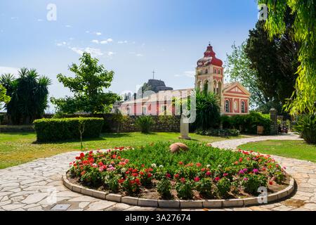 Rote Heilige Kirche der Jungfrau Maria Mandrakina auf dem Mandrakinas Platz, neben der alten Festung von Korfu in Korfu Stadt mit üppigem Blumengarten davor Stockfoto