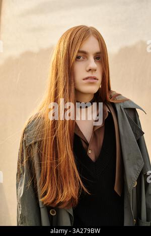 Ein junger, gutaussehender Mann mit langen Haaren steht selbstbewusst und strahlt Mode und Eleganz aus. Stockfoto