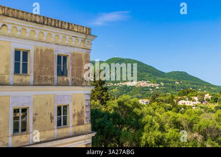 Panoramablick auf den Achilleion Palast mit dem Dorf Agii Deka am Hang des Berges und weißem Rundradar auf der Spitze der Insel Korfu, Griechenland Stockfoto