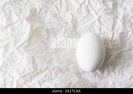 Weiße Eier auf zerknittertem Papier, die eine minimalistische und rustikale Komposition schaffen. Weiches Tageslicht hebt Texturen hervor und ist somit ideal für Easte Stockfoto