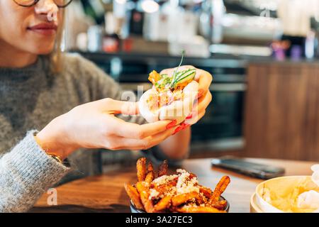 Frau, die ein Gourmet-bao-Brötchen in einem modernen Café genießt Stockfoto
