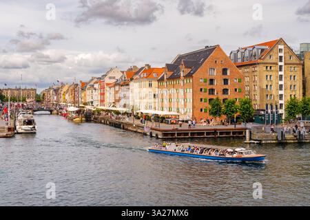 Sightseeing-Boot mit Touristen, die den Nyhavn-Kanal verlassen, historische Lagerhäuser und Kanalhäuser im Hintergrund, Kopenhagen, Dänemark Stockfoto