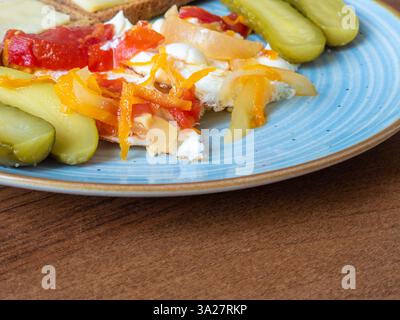 Hell überzogene Spiegeleier stehen neben lebendigen eingelegten Gurken und bunten Karotten mit rotem Pfeffer, was ein fröhliches Frühstück auf einem Charmi schafft Stockfoto