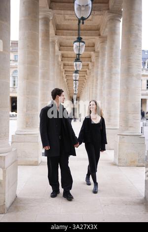 Ein stilvolles Paar in schwarz gekleidet schlendert Hand in Hand durch die große Kolonnade des Palais-Royal in Paris und vereint Liebe, Eleganz und zeitlosen französischen Charme. Stockfoto