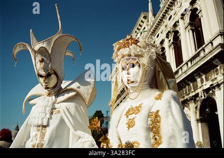 Zwei elegant gekleidete Figuren in aufwendigen Kostümen und Masken, die komplexe Designs und Goldverzierungen vor einem klaren blauen Himmel und Histoire zeigen Stockfoto