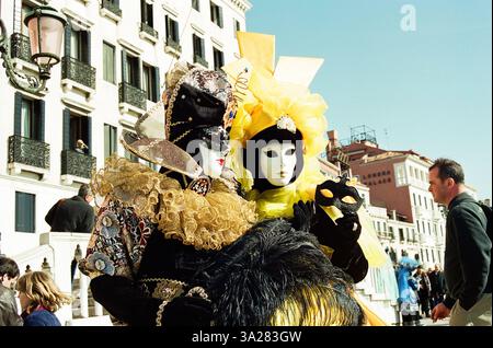 Zwei Personen in ausgeklügelten Masken und Kostümen posieren für ein Foto während eines Festivals in Venedig, Italien. Die lebendigen Farben und das komplizierte Design ihrer Stockfoto