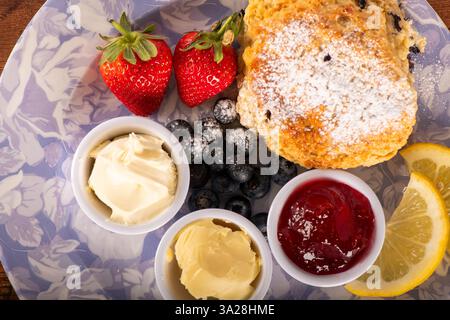 Ein Teller mit einem Zitronenkeil, Erdbeeren, Heidelbeeren und Marmelade. Die Platte ist blau und weiß Stockfoto