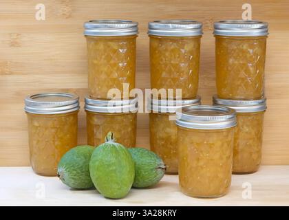 Schließen Sie ein Glas frischer hausgemachter Marmelade mit frisch reifer Feijoa sellowiana, auch bekannt als Acca sellowiana Burret oder Ananas-Guava. Heller Holztisch mit Stockfoto