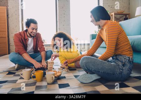 Gruppe von Freunden, die bei Tageslicht in einem gemütlichen Wohnzimmer zusammen ein Holzblockspiel spielen, genießen Freizeit und Freundschaft Stockfoto