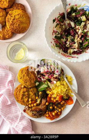 Ein reichhaltiges, ausgewogenes Frühstück mit Linsen- und Zucchini-Pfannkuchen, Hirse, gebackenem Hähnchenhals, gerösteten Süßkartoffeln, Brokkoli, Karotten, Kichererbsen und Stockfoto