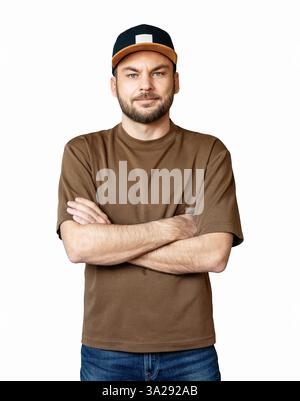 Vorderansicht Porträt eines jungen Erwachsenen kaukasischen Mannes mit kurzem Bart, braunem T-Shirt und Snapback, stehend mit überkreuzten Armen isoliert auf weißem Rücken Stockfoto