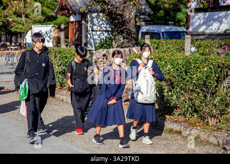 Japanische Schulkinder in Uniform laufen durch einen Park in Kyoto, Japan. Stockfoto