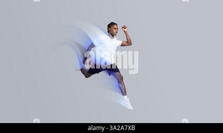 Dynamischer Mann in Sportbekleidung, der auf grauem Studiohintergrund läuft Stockfoto