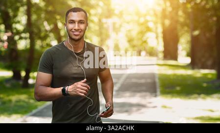 Fröhlicher Jogger mit Handy, Musik hören und genießen seinen Lauf im Park am sonnigen Morgen Stockfoto