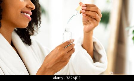 Schönheitsbehandlung Zu Hause. Lächelnde Afrikanische Frau Öffnungsflasche Mit Feuchtigkeitsspendenden Serum Stockfoto