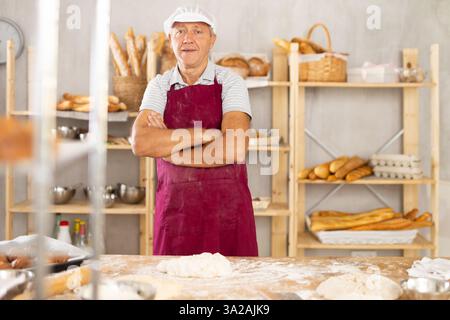 Senior Mann arbeitet in der Bäckerei als Bäcker, Knete Teig, arbeitet mit Mehl. Stockfoto