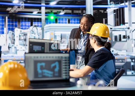 Mitarbeiter in der Photovoltaik-Fabrik überprüfen Systemprotokolle, um betriebliche Ineffizienzen zu identifizieren. Manager und Arbeiter einer photovoltaikanlage in Afrika, die Herstellungsparameter am PC anpassen Stockfoto
