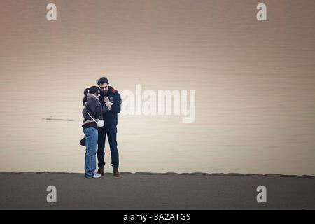BELGRAD, SERBIEN - 12. OKTOBER 2024: Ein Paar, das ein Smartphone an der Donau in Zemun, Belgrad, benutzt, um moderne Beziehungen zu veranschaulichen Stockfoto