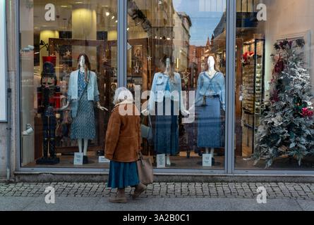Ältere Frau in braunem Mantel und blauem Kleid, die stilvolle Schaufensterpuppen in einer Mode-Boutique ansieht. Stockfoto