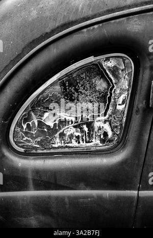 Die Heckscheibe eines rostigen Autos ist mit einer Form von Korrosion beschlagen. In Schwarzweiß. Stockfoto