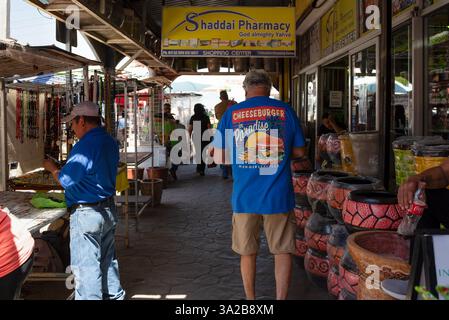 Mann mit blauem Margarataville Cheeseburger in Paradise T-Shirt geht den Bürgersteig mit Händlern entlang, Nuevo Progreso, Mexiko, USA. Stockfoto