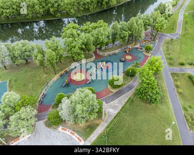 Farbenfroher Kinderspielplatz im öffentlichen Park, umgeben von grünen Bäumen. Sommerzeit. Luftaufnahme. Stockfoto