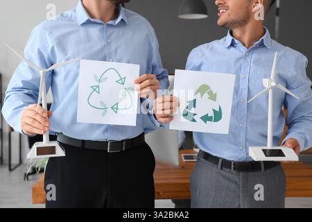 Männliche Ingenieure, die mit Windkraftanlagenmodellen arbeiten und Schilder im Büro recyceln, Nahaufnahme Stockfoto