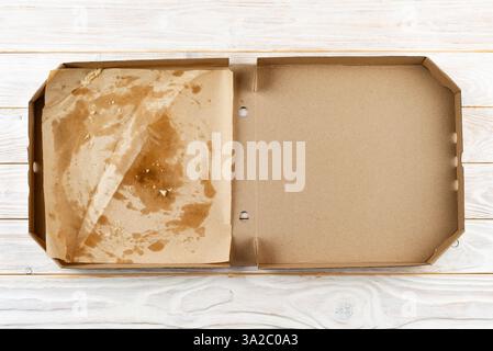 Leere Pizzaschachtel mit Brotkrumen auf weißem Holztisch mit flacher Ladefläche Stockfoto