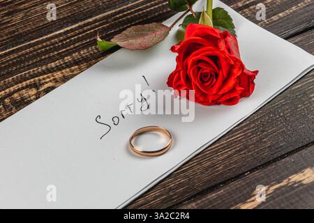 Eine herzliche Botschaft auf einem Blatt Papier drückt die Trauer über eine gebrochene Verlobung aus. Ein goldener Ring und eine leuchtende rote Rose begleiten die Note „RESTI“ Stockfoto