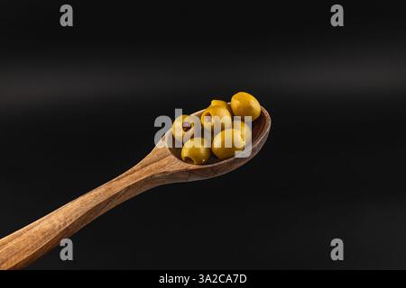 Ein Holzlöffel fasst mehrere grüne Oliven und zeigt ihre reichhaltige Textur und Farbe. Die Präsentation hebt die natürliche Schönheit der Oliven wieder hervor Stockfoto