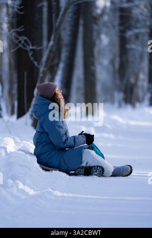 Junge Frau in warmer Winterkleidung sitzt auf einem Schneeschlitten, umgeben von einem malerischen verschneiten Wald, genießen die frische Luft und genießen die Ruhe der Natur Stockfoto