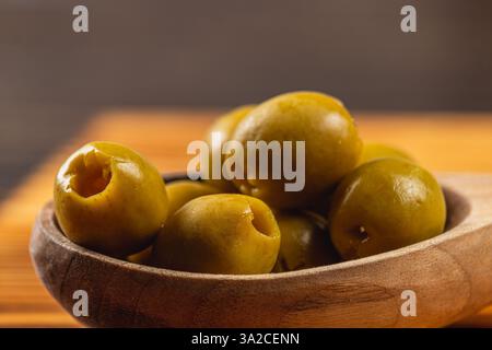 Frisch geerntete grüne Oliven werden wunderschön in einer rustikalen Holzschale präsentiert, die der gemütlichen Kücheneinrichtung einen Hauch von Wärme und Komfort verleiht. Stockfoto