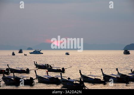 Ein atemberaubender Sonnenuntergang über dem ruhigen Meer am Ao Nang Beach, Thailand, mit Booten, die auf dem Wasser schwimmen, und fernen Inseln, die eine atemberaubende Silhouette schaffen Stockfoto