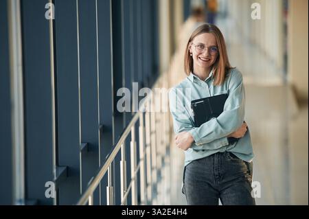 Fröhlicher Gesichtsausdruck, mit schwarzem Tablet. Junge Frau in der Flughafenhalle. Stockfoto