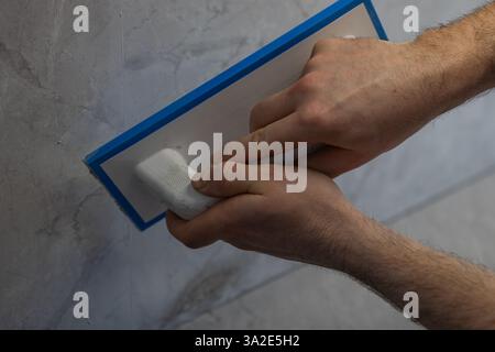 Arbeiter, der während der Wandverkleidung Fugen auf Keramikfliesen mit einem Gummischwimmer aufträgt. Handpresse zum Füllen von Lücken zwischen Fliesen in Marmoroptik Stockfoto