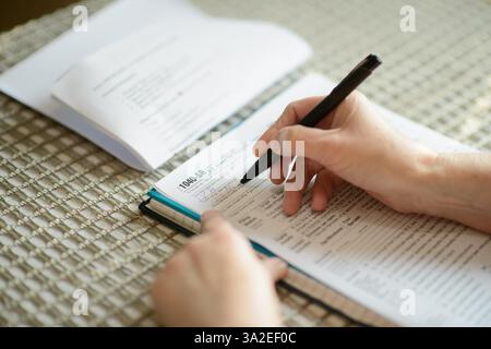 Eine ältere Frau, die an einem Tisch saß und ihr Steuerformular 1040-SR sorgfältig mit einem Stift ausfüllte. Das Home-Setting unterstreicht die persönliche Finanzorganisation Stockfoto
