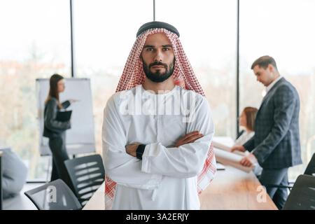 Vor Leuten zu stehen, die dahinter stehen. Muslimischer Geschäftsmann in traditioneller Kleidung mit Kollegen im Amt. Stockfoto