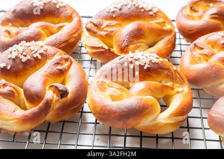 Appetitliche Brezeln, Brezeln oder Brötchen mit grobem Salz auf einem schwarzen Grill auf weißem Hintergrund. Draufsicht. Flache Lagen. Nahaufnahme. Hochwertige Fotos Stockfoto