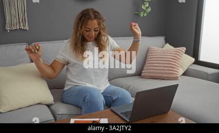 Die junge Frau saß auf einem gemütlichen Wohnzimmersofa drinnen und setzte sich mit einem Laptop auf einem Holztisch ein, der mit einem modernen Apartment-Interieur ausgestattet war Stockfoto