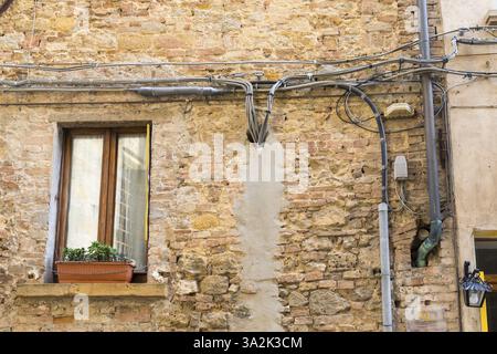 Hauswand mit freiliegenden Stromkabeln, Löchern und teilweise verputzt im historischen Zentrum von Volterra, Provinz Pisa, Toskana, Italien, Europa Stockfoto