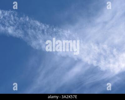 Auflösung diagonaler Kondensstreifen eines Jet-Flugzeugs hinter weißen Wolken Cirrostratus-Schleier-Wolken vor blauem Himmel, international Stockfoto