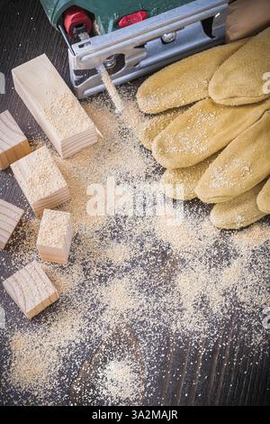 Satz von elektrischen Stichsägen-Sägespäne-Leder-Arbeitshandschuhen und Holznieten auf Vintage-Holz-Hintergrund-Konstruktionskonzept Stockfoto