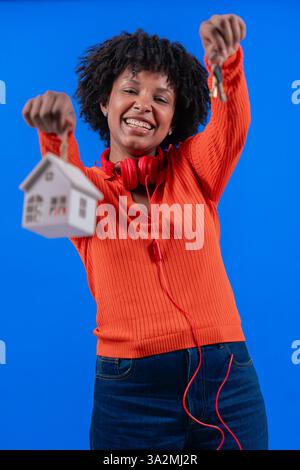 Afroamerikanerin, die Hausschlüssel und Hausmodel hält und selbstbewusst lächelt Stockfoto