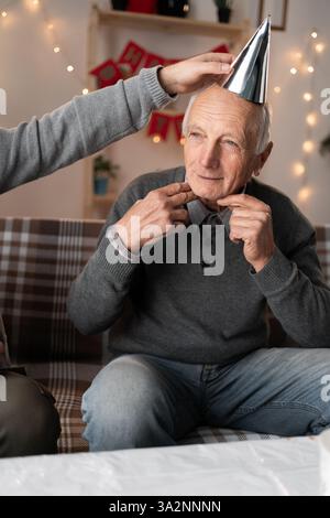 Senior-Mann mit Partyhut, der zu Hause auf der Couch sitzt Stockfoto