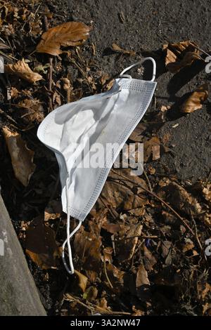 Gesichtsmaske, PSA-Ausrüstung, getragen und dann in der Rinne mit Blättern als moderner Müll entsorgt Stockfoto