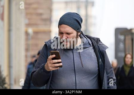 Fette Mann mit Smartphone, der die Straße der Stadt entlang läuft Stockfoto
