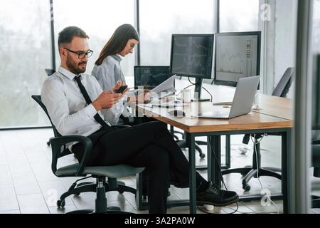 Der Mann benutzt ein Smartphone. Zwei Mitarbeiter arbeiten gemeinsam im Büro. Stockfoto