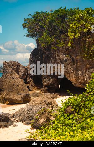 Korallenhöhle bedeckt mit Laub mit großen Felsen an einem Sandstrand am weißen Strand, boracay. Stockfoto